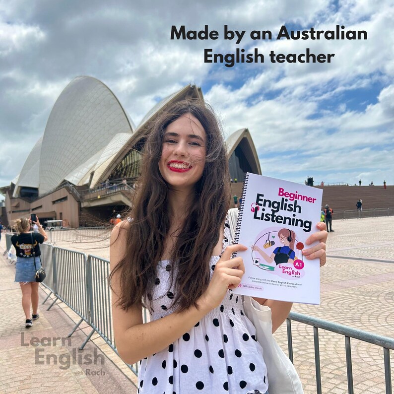 May include: A woman in a white and black polka dot dress holds a book titled "Beginner English Listening" with the text "Learn English A1" on the cover. The book is in front of the Sydney Opera House.