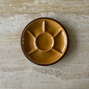May include: A round, divided serving dish with a glossy, golden-brown glaze. The dish has a dark brown rim and is sectioned into six compartments, perfect for serving appetizers or snacks. The dish is made of ceramic.