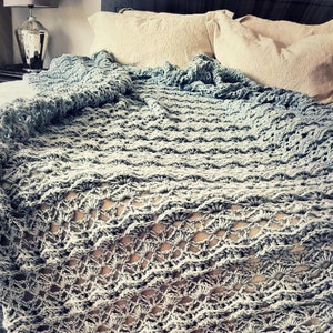 May include: A light blue crocheted throw blanket with a delicate openwork pattern. The blanket is draped over a bed with white pillows.