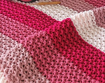 May include: A crocheted blanket with a gradient of pink, red, and white stripes. The blanket is made with a delicate stitch pattern and is perfect for a baby or child.