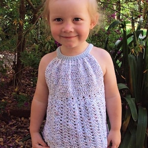May include: A young girl wearing a white crocheted halter top with a light blue trim. The top has a scalloped hem and is worn over blue jeans.
