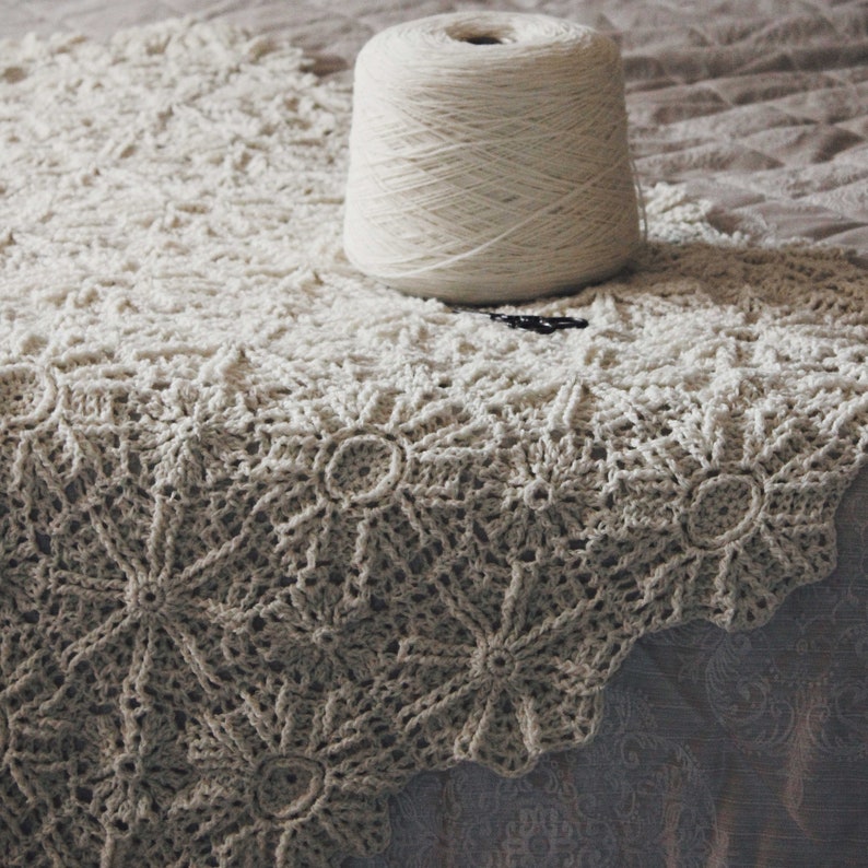 Puede incluir: Una manta de crochet blanca con un delicado patr&oacute;n floral. La manta est&aacute; hecha con un hilo suave y ligero y tiene un sutil efecto degradado.