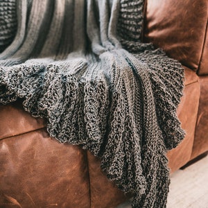 Peut inclure: Une couverture en tricot gris avec un motif texturé est jetée sur un canapé en cuir brun.