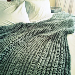 May include: A green crocheted throw blanket draped over a bed with white pillows.