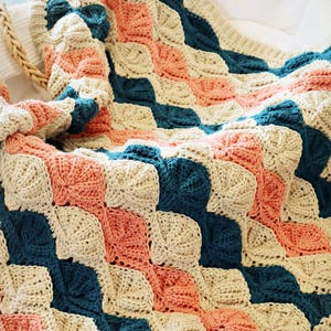 May include: A handmade crochet blanket with a geometric pattern of squares in coral, teal, and cream. The blanket is made of soft yarn and has a textured appearance, suitable for home decor.