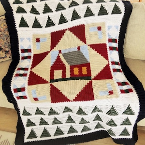May include: A crocheted throw blanket with a patchwork design featuring a red, white, and blue house with a green roof. The blanket has a black border with green triangles on a white background.