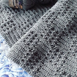 May include: A grey knitted blanket with a textured pattern. The blanket is made with organic cotton yarn and is shown with balls of yarn.