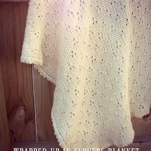 May include: A white crocheted blanket with a delicate pattern, draped over a wooden fence. The blanket is called "Wrapped Up In Clovers Blanket" and is designed by Lisa van Klaveren.