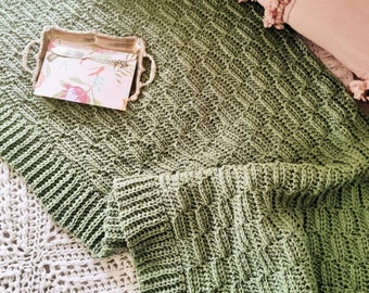 May include: A green crocheted throw blanket with a textured pattern. The blanket is folded and draped over a white crocheted blanket.