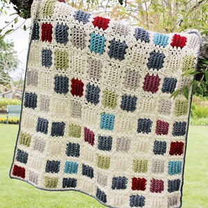 May include: A square crochet blanket featuring a grid of cream-colored yarn squares interspersed with solid blocks of red, dark blue, light blue, and olive green. The blanket has a textured, open-stitch pattern and a dark gray border along the edges.