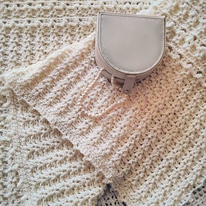 May include: A cream-colored crocheted blanket with a small, light beige, round jewelry box with a chain attached.