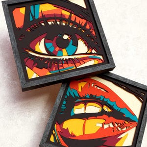 Op de afbeelding: Twee vierkante ingelijste meerlaagse kunstwerken met pop-art ontwerpen van een oog en lippen. Het kunstwerk gebruikt zwarte, rode, gele en blauwgroene lagen voor diepte. De tekst bovenaan luidt studio TOKANO Cricut & Laser SVG Cut File.