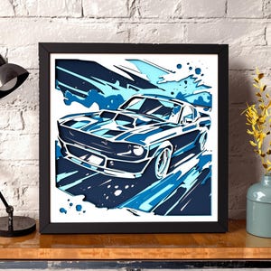 May include: A square framed wall art piece featuring a stylised illustration of a classic muscle car in shades of navy blue, light blue, and white. The artwork uses layered cut-out shapes to create a sense of motion and depth for the vehicle.