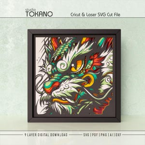 May include: A square black frame containing a multi-layered paper art design of a stylized dragon head. The artwork features intricate cutouts in shades of green, yellow, orange, and red against a dark background. Text reads studio TOKANO.