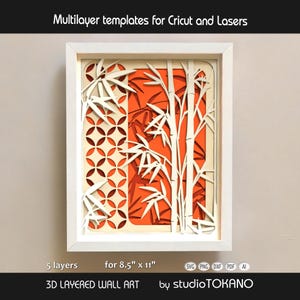 May include: A 3D layered wall art piece in a white frame featuring bamboo stalks and a geometric circle pattern. The design uses five layers of white and cream paper against a vibrant orange background. Text reads Multilayer templates for Cricut and Lasers, 5 layers for 8.5" x 11", 3D LAYERED WALL ART, and by studioTOKANO.