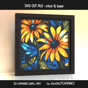 May include: 3D layered wall art featuring two stylized orange and yellow flowers with blue and green leaves, set against a dark background. The artwork is framed in a dark brown square frame. Text at the top reads "SVG CUT FILE - cricut & laser".