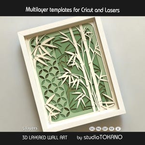May include: A 3D layered wall art piece in a white frame featuring five layers of cut-out bamboo stalks and a geometric circular pattern. The design uses shades of cream and sage green. Text includes Multilayer templates for Cricut and Lasers.
