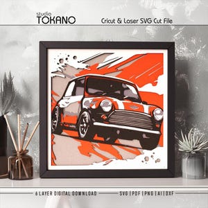 May include: A multi-layered paper art piece in a black frame featuring a classic Mini Cooper car design. The artwork uses orange, white, and black layers to create a dimensional effect. The text Studio TOKANO and Cricut & Laser SVG Cut File appear.