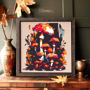 Op de afbeelding: Een vierkant ingelijst kunstwerk aan de muur met een illustratie in gelaagde papierknipstijl van rode en oranje paddenstoelen met witte stippen tegen een donkerblauwe achtergrond. De tekst studio TOKANO staat in het midden bovenaan.