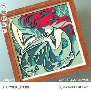 Op de afbeelding: Een 3D gelaagd wandkunstwerk met een zeemeermin met rood haar en een turquoise en witte staart. De zeemeermin wordt omringd door bladeren en de kunst is ingelijst in een houten lijst. De tekst "CARDSTOCK Collection" en "by studioTOKANO.com" is zichtbaar onderaan de afbeelding.