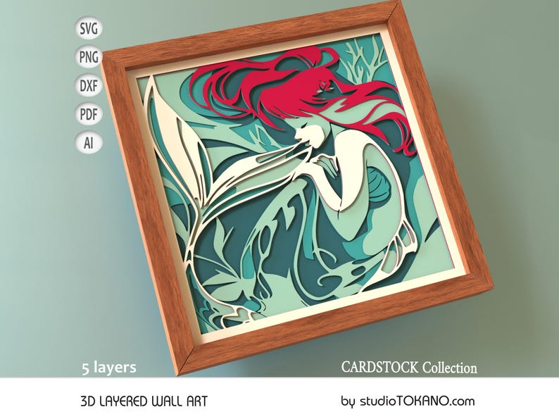 Op de afbeelding: Een 3D gelaagd wandkunstwerk met een zeemeermin met rood haar en een witte staart. De zeemeermin is omringd door turquoise en groen gebladerte. De kunst is ingelijst in een houten lijst en heeft 5 lagen. CARDSTOCK Collection van studioTOKANO.com