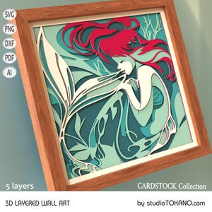 Op de afbeelding: Een 3D gelaagd wandkunstwerk met een zeemeermin met rood haar en een witte staart, omringd door turquoise en groen gebladerte. De kunst is ingelijst in een houten lijst en heeft de tekst "CARDSTOCK Collection" en "by studioTOKANO.com" onderaan.