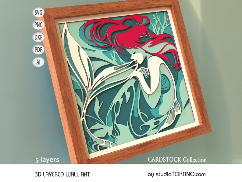 Op de afbeelding: Een 3D gelaagd wandkunstwerk met een zeemeermin met rood haar en een witte staart, omringd door turquoise en groen gebladerte. De kunst is ingelijst in een houten lijst en heeft de tekst "CARDSTOCK Collection" en "by studioTOKANO.com" onderaan.