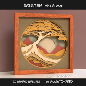 May include: A framed 3D layered wall art piece. The circular design depicts a tree, mountains, and sun, crafted from layered paper in shades of brown, beige, and orange. The frame is wooden. Text on the image reads "SVG CUT FILE - cricut & laser".