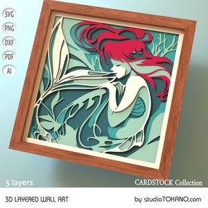 Op de afbeelding: Een 3D gelaagd wandkunstwerk met een zeemeermin met rood haar en een turquoise staart. De zeemeermin is omringd door bladeren en is ingelijst in een houten lijst. Het kunstwerk is gelabeld met "CARDSTOCK Collection" en "studioTOKANO.com".