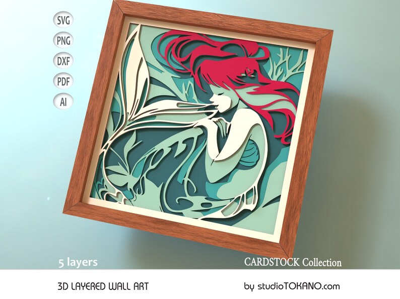 Op de afbeelding: Een 3D gelaagd wandkunstwerk met een zeemeermin met rood haar en een turquoise staart. De zeemeermin is omringd door bladeren en is ingelijst in een houten lijst. Het kunstwerk is gelabeld met "CARDSTOCK Collection" en "studioTOKANO.com".