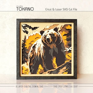 May include: A multi-layered paper art piece in a black frame featuring a bear in a forest setting. The design uses shades of brown, black, and yellow to create depth. Text at the top reads studio TOKANO Cricut & Laser SVG Cut File.