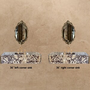 May include: Two 36-inch corner sinks with marble worktops and ornate gold mirrors above them. The sinks are made of a light brown and purple marble with dark veins.