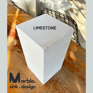 May include: A close-up of a white, rectangular block of limestone. The block is sitting on a wooden surface. The text "LIMESTONE" is printed on the top of the block.