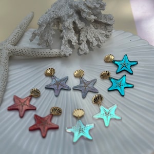 May include: A set of six pairs of earrings featuring a starfish design. The earrings are made of gold-tone metal and have a variety of colours, including blue, pink, and red.