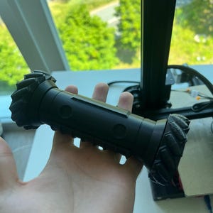 May include: A black 3D printed object with a textured surface and two circular holes. The object is shaped like a cylinder with rounded ends.