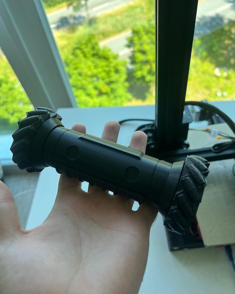 May include: A black 3D printed object with a textured surface and two circular holes. The object is shaped like a cylinder with rounded ends.