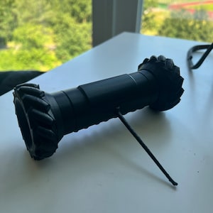 May include: A black 3D printed gear with a thin black string attached to it.