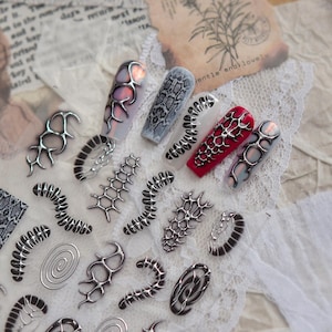 May include: A collection of nail art designs featuring various styles. Some nails are painted with snake skin patterns, while others have a red base with silver accents. Silver metal nail art pieces are also displayed.