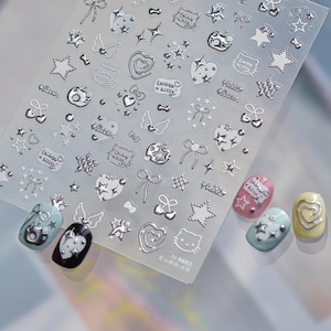 May include: Silver nail art stickers featuring stars, hearts, bows, and cat faces. Several manicured nails are shown with the stickers applied, demonstrating the designs. The sheet has text in Chinese.