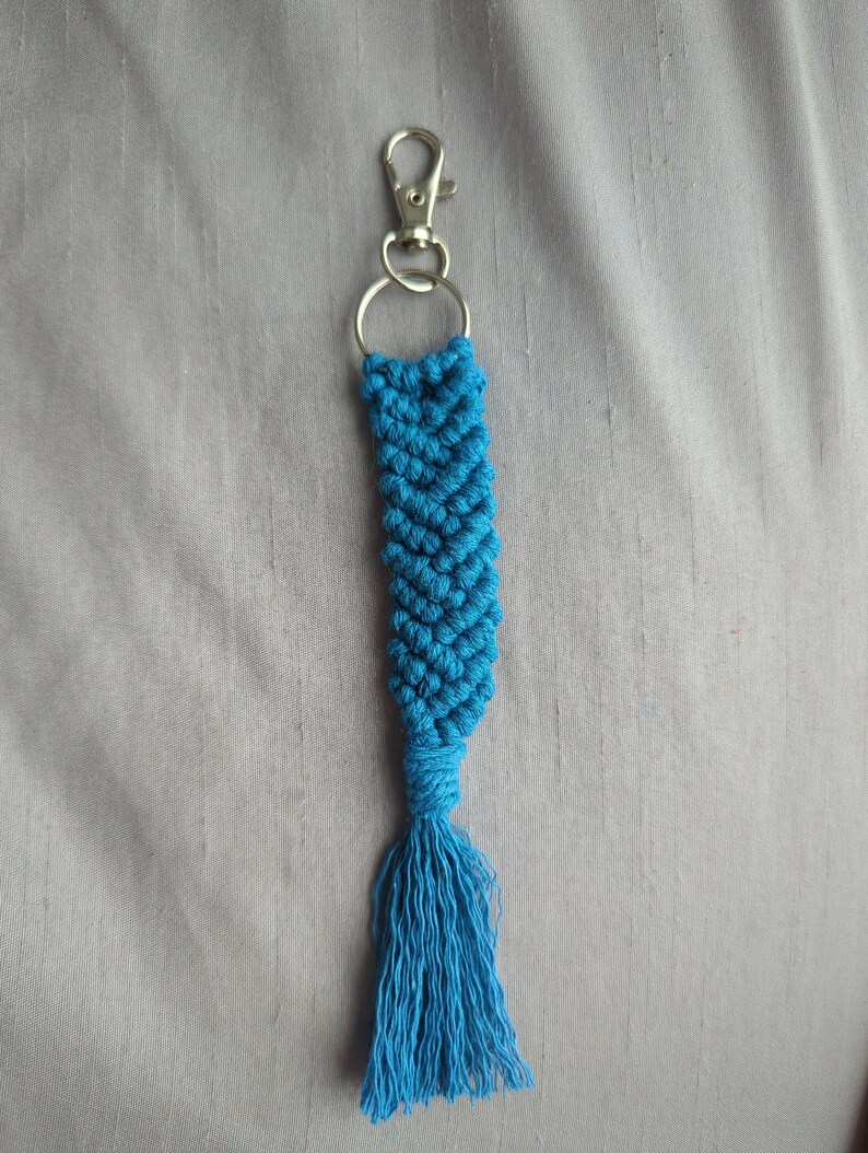 May include: A blue macrame keychain with a silver key ring and a tassel.