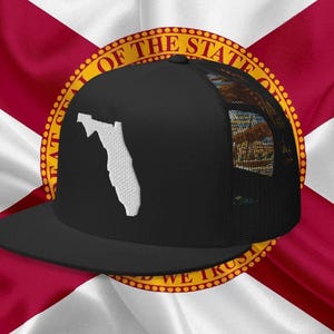 May include: Black trucker hat with a white outline of the state of Florida on the front. The hat is on top of a Florida state flag with the state seal.