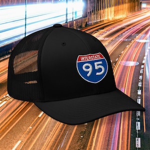May include: Black trucker hat featuring the Interstate 95 logo. The logo is a white number 95 inside a blue shield with a red border and the word "Interstate" above. The hat has a mesh back and a curved brim.