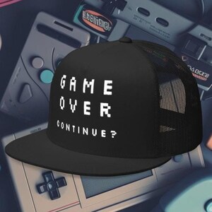 May include: Black and white trucker hat with a black mesh back. The hat has the text "GAME OVER CONTINUE?" in white pixelated letters.