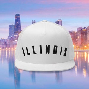 May include: A white trucker hat with the word "ILLINOIS" in black, arched text. The hat has a mesh back and a curved brim. The background features a cityscape with tall buildings and a body of water.