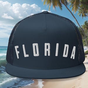 May include: A navy blue trucker hat with a white mesh back. The hat has the word "FLORIDA" embroidered in white on the front.