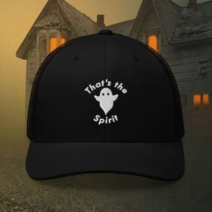 May include: Black trucker hat with a white embroidered ghost and the text "That's the Spirit." The hat has a mesh back and a curved brim. The design is centered on the front of the hat.
