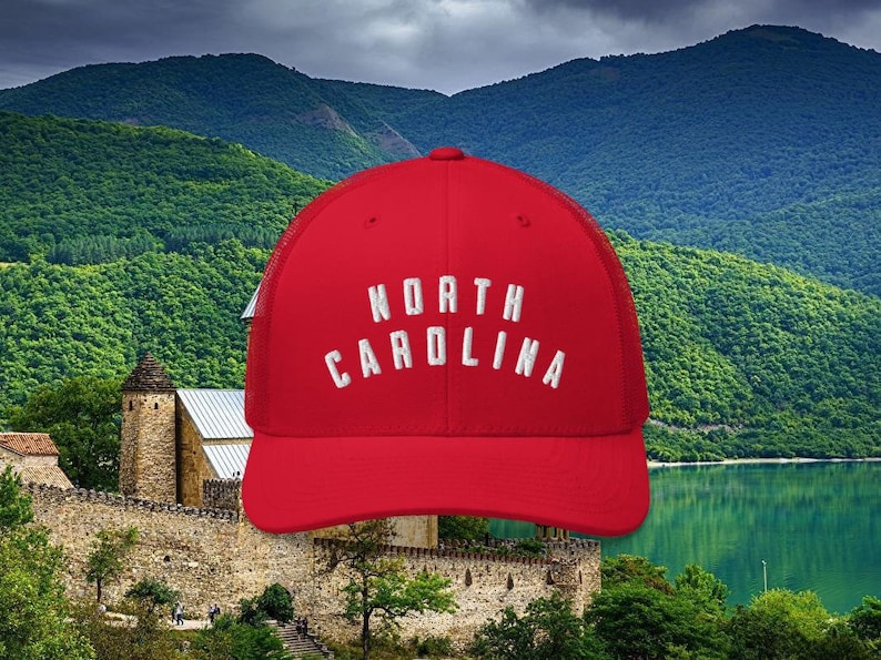May include: Red trucker hat with a white mesh back and white embroidered text that reads "NORTH CAROLINA".