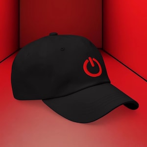 May include: Black baseball cap with a red power button logo on the front. The cap has a curved brim and a rounded crown. The background is a solid red.