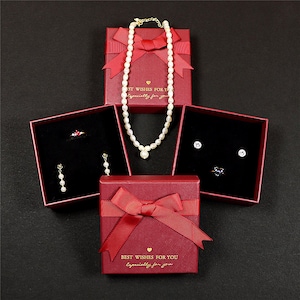 May include: An overhead shot of jewelry displayed in red gift boxes with bows. The boxes contain a pearl necklace, earrings, a ring, and stud earrings. The boxes have the text "Best Wishes For You, Especially For You."