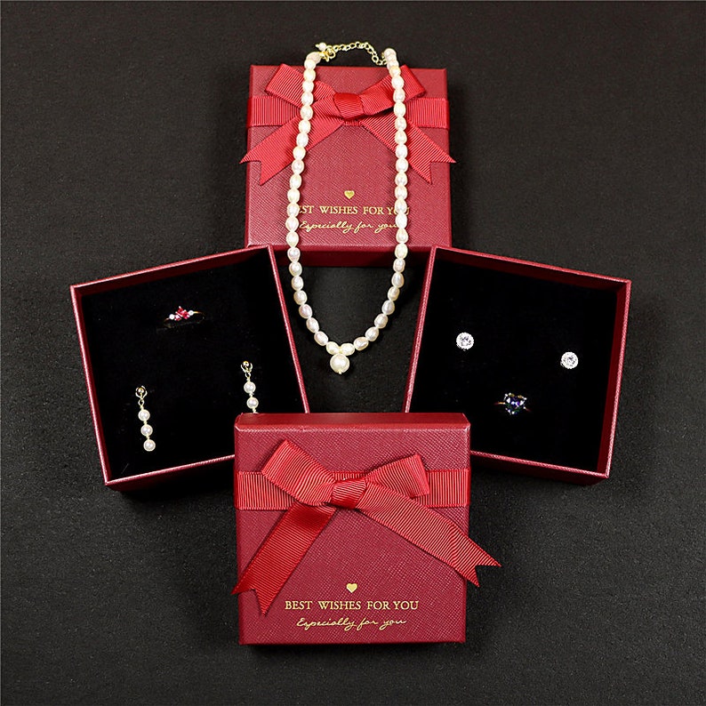 May include: An overhead shot of jewelry displayed in red gift boxes with bows. The boxes contain a pearl necklace, earrings, a ring, and stud earrings. The boxes have the text "Best Wishes For You, Especially For You."